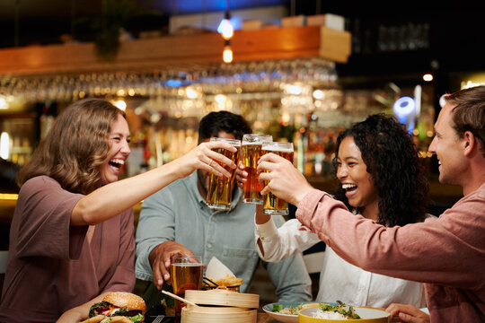 Young multiracial group of friends in casual clothing celebrating with drinks and dinner at restaurant