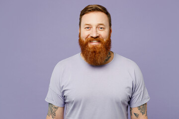 Young smiling cheerful fun happy cool redhead bearded man he wear violet t-shirt casual clothes looking camera isolated on plain pastel light purple wall background studio portrait. Lifestyle concept.