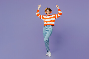 Full body happy smiling cheerful young woman wear casual clothes sweatshirt headphones listen to music dance raise up hands isolated on plain pastel light purple background studio. Lifestyle concept.