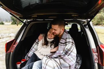 a couple in love sits in the trunk of a car. travel by car in the mountains and near the river. autumn journey during the rain. picnic in the car