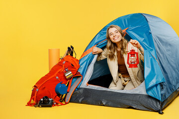 Full body young woman sit near bag with stuff tent hold lantern look aside isolated on plain yellow background. Tourist leads active lifestyle walk on spare time. Hiking trek rest travel trip concept.