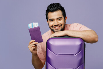 Traveler Indian man wear casual clothes hold suitcase passport ticket isolated on plain purple...