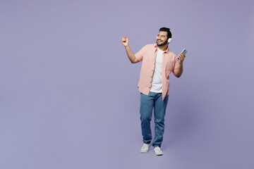 Fototapeta na wymiar Full body young happy Indian man wear pink shirt white t-shirt casual clothes headphones listen music use mobile cell phone isolated on plain pastel light purple background studio Lifestyle concept