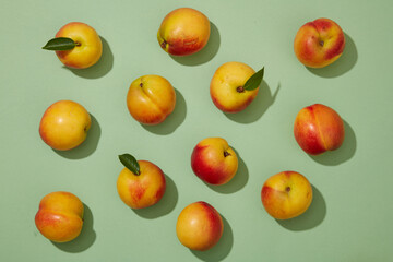 Top down flat lay colorful shot with fresh ripe peaches (prunus persica) on pastel green background. Minimal scene for advertising product with peach ingredient.