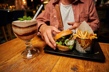 Close-up of young caucasian man in casual clothing with burger and chips on table at restaurant