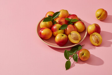 A dish of many fresh peaches put on light pink background. Copy space. Peach (Prunus persica)...