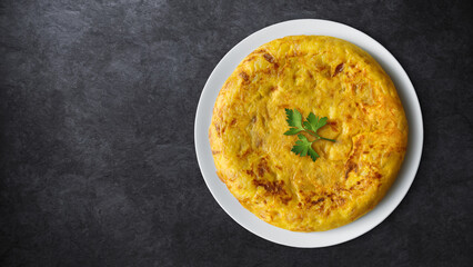 Potato and onion omelette in a plate on a dark stone background