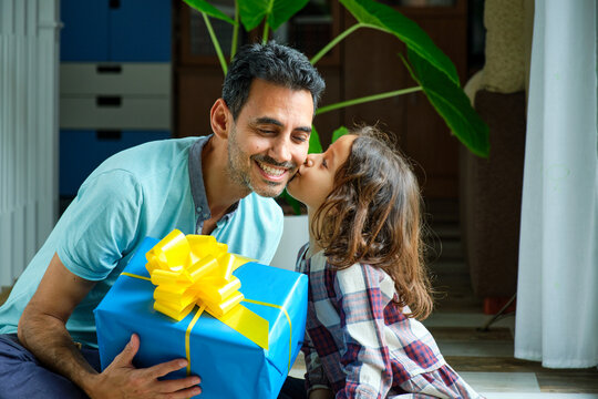 little girl giving a kiss to her father who is smiling for having received a gift