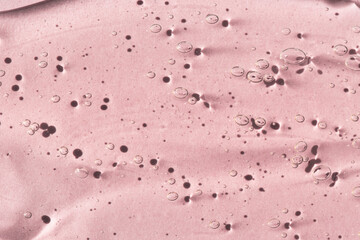 Transparent cosmetic texture of serum, skin gel on a pink background, macro top view.