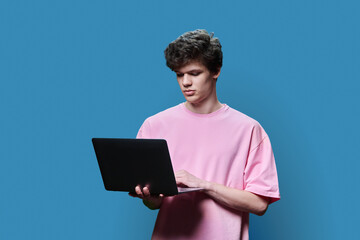 Young male college student using laptop, blue studio background
