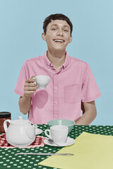 Young happy boy sitting at table, having breakfast and smiling over white studio background. Rainbow style palette. Concept of emotions, retro style
