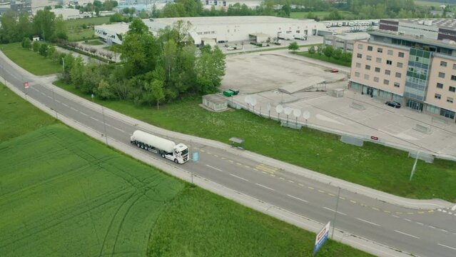 Fuel truck riding on road to distribution warehouse in city suburbian area aerial shot. Tanker lorry driving on highway near industrial building and country field