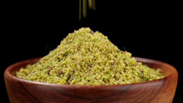 Pistachio flour falling in wooden bowl, black background. Ground pistachio ingredient for dessert and bakery product