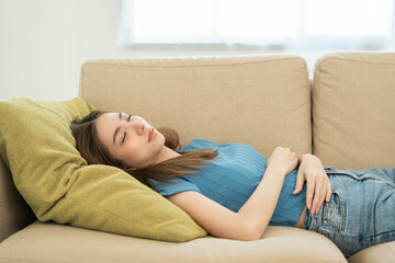 Fototapeta premium Asian caucasian woman lying on comfortable sofa in living room. Asian female fall asleep take a nap. Exhausted tired young woman. Cozy couch breath fresh air inside modern living room Leisure