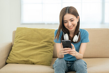 Relaxing time in living room. Beautiful young asian woman choose music from smartphone take a rest and listening song with headphone and dancing. Lifestyle in living room at house in the morning.