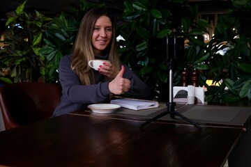 A woman is talking on a video chat in a cafe using a smartphone. communication, online communication, emotions and gestures.