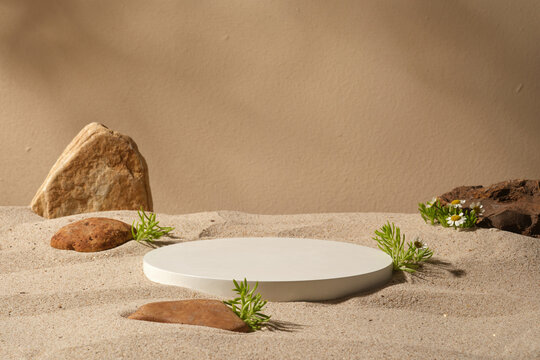 A white podium in round-shaped placed on the beach sand with some stones. Modern minimal showcase scene for cosmetic products promotion