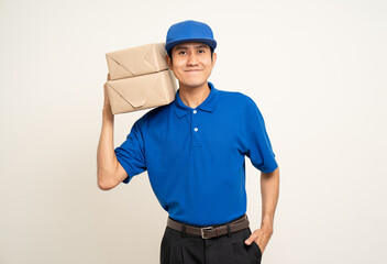 Happy delivery asian man in blue uniform standing holding box parcel cardboard on isolated white background. Smiling male service worker. Delivery courier and shipping service.