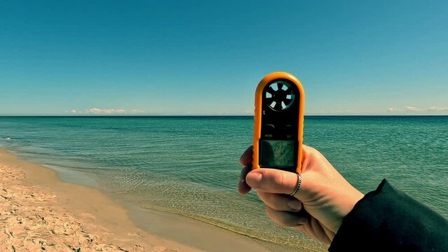 Wind force measurement. Female hand holding a device for measuring wind strength on the sea beach. Anemometer.