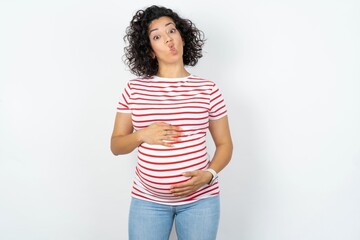 Beautiful pregnant woman wearing striped T-shirt standing over white studio background making fish...