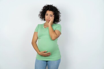 Sad lonely Beautiful pregnant woman wearing green T-shirt standing over white studio background...
