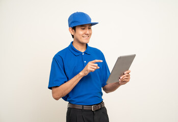 Asian man in blue uniform standing holding digital tablet computer on isolated white background. Male service worker with cell phone. Delivery courier shipping service