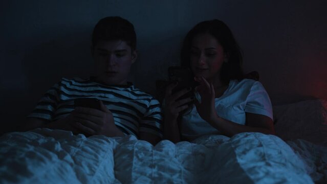 Young couple using social media together instead of going to sleep in bed