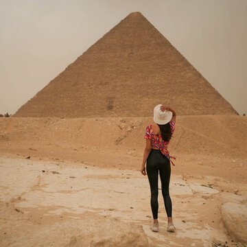 Young Beautiful Tall Girl in front of the Egyptian pyramid of Giza in white straw hat with storm approaching