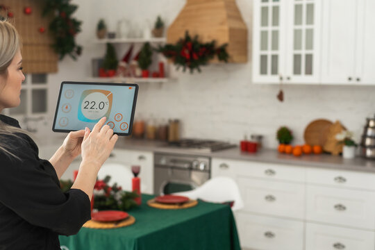 Woman pushing button on kitchen app of smart home on digital tablet at home. Concept of modern home control. Idea of domestic lifestyle. Cropped image of girl. Blurred man on background using laptop.