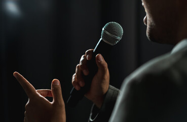 Confident successful speaker man talking on stage with spotlight strike through the darkness at...