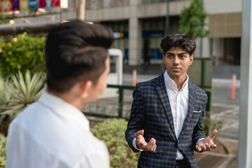A young indian man debates or explains his opinion to his colleague while outside the office. An...