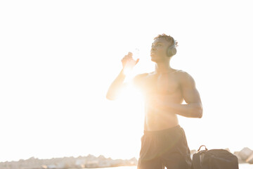 Young athlete man listening music while resting after training. Handsome African man training outside