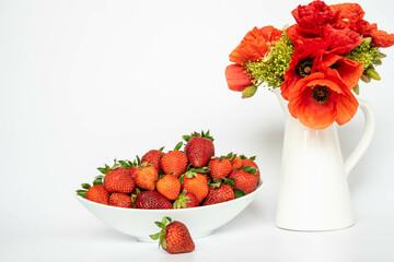 Strawberries in a white ceramic tray, near a white vase with blooming poppies, on a white background