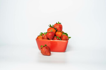 Strawberries in a red ceramic heart shaped pot, on a white background