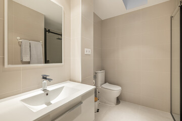 Fototapeta na wymiar Stylish spacious bathroom with toilet, shower and sink with cabinet and mirror in beige tones in a new building. Concept of convenient and concise renovation in the bathroom. Copyspace