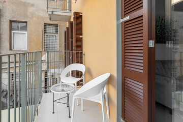 Table and chairs stand on an unglazed balcony overlooking the courtyard and other balconies and fire escapes of the house. The concept of relaxation and fresh air without leaving home - obrazy, fototapety, plakaty