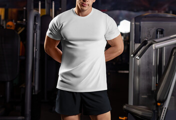 White sports t-shirt mockup on a sports guy with hands behind his back, shirt on an athlete in the gym, front view.