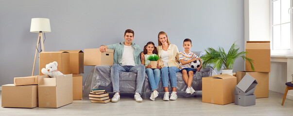 Happy family in new home on moving day. Smiling mom, dad, son and daughter sitting on sofa in...