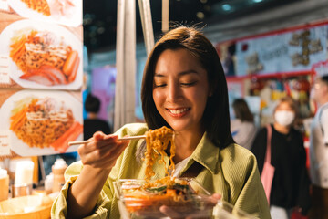 Asian woman enjoy eating noodles street food at night market. Traveler Asian blogger women Happy tourists Beautiful female with Traditional thailand bangkok food.