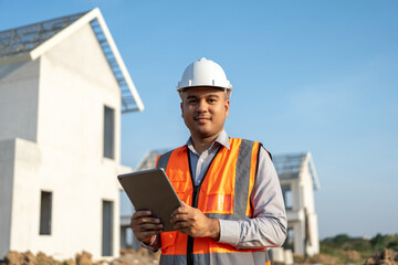 Confident asian engineer man Using tablet for checking and maintenance to inspection at modern home building construction. Architect working with white safety helmet in construction site