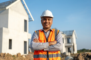 Confident engineer handsome man at modern home building construction. Architect with white safety helmet at site. Real Estate building under construction. Foreman senior worker project designer