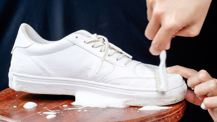 A Woman cleaning white leather shoes with cleaning foam. The concept of caring for leather footwear