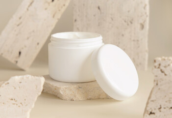 Fototapeta na wymiar Opened white cream jar with a lid near biege stones close up. Cosmetic Mockup