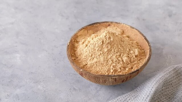 Top view of a bowl with raw maca root powder on light grey background with copy space