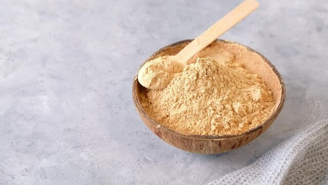 Top view of a bowl with raw maca root powder on light grey background with copy space