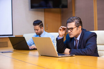 Indian businessman giving unhappy expression after looking in laptop at office.