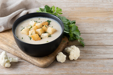 Cauliflower soup in a bowl on wooden table. Copy space