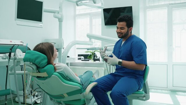 Positive indian dentist man consults patient in hospital. Dentist appointment