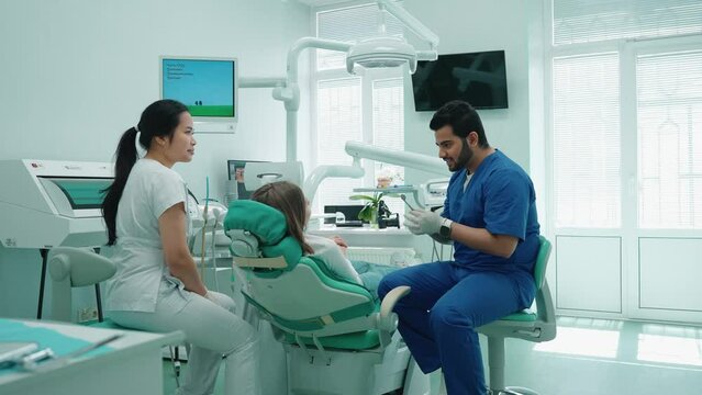 Positive indian dentist man consults patient before procedure in hospital. Dentist appointment