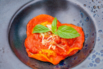 Closeup of tasty ravioli with tomato sauce, cheese, and basil on black plate in Italian restaurant. A delicious Italian dish to enjoy in restaurant setting.